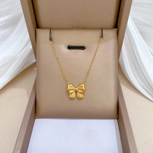 Golden bow pendant necklace in a beige gift box with white silk fabric background