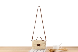 Detail view of woven straw crossbody bag with metal lock on light wood surface
