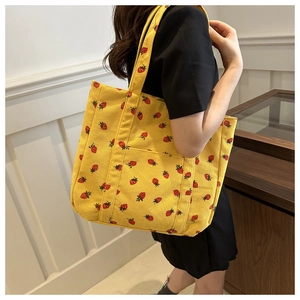 Detail of yellow corduroy tote bag featuring red strawberry print and exterior pocket