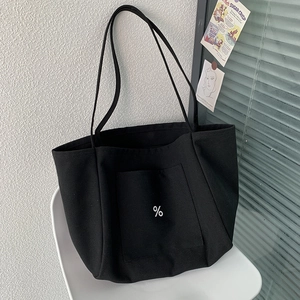 Detail of a thick black canvas tote bag with a white % logo on a white chair