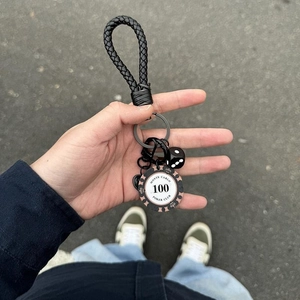 Macro detail of black braided leather keychain with Monte Carlo poker chip and dice charm