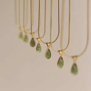 Detail of water drop emerald pendant on gold snake chain with minimalist French style