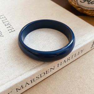 Detail of a thick dark blue resin round bangle with a smooth glossy finish on a book