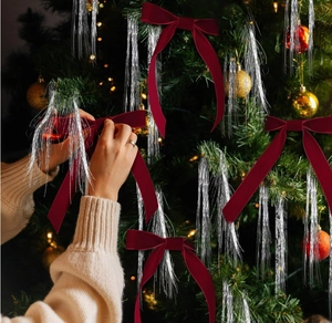 Close-up of deep red velvet bow and silver fringe being placed on a lit Christmas tree