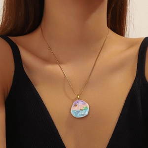 Detail of a gold stainless steel necklace with a colorful painted shell pendant on a model