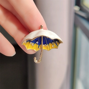Macro detail of enamel umbrella brooch with rhinestones held by hand near a window