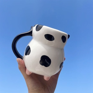 Detail of 3D cow shaped ceramic mug with black spots and pink feet against blue sky