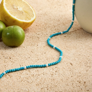 Blue natural stone and white bead beaded necklace on a stone background with lemons