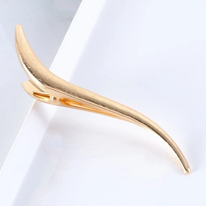 Polished gold S-shaped curved metal hair clip on white tray minimalist display