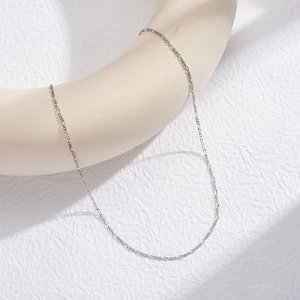 Detailed view of a slender S925 sterling silver Figaro chain on a white display