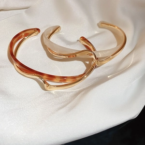 Detail of wavy gold metal bangles with amber and ivory resin inlays on white silk