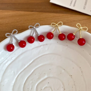 Detailed macro shot of red cherry earrings with bow accents on a white ceramic plate