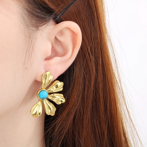 Close-up of a 18K gold flower earring with a round turquoise stone on a model