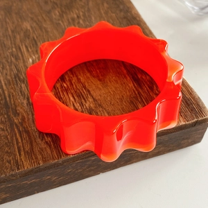Close-up of vibrant orange wavy resin bangle on a textured dark wood block pedestal