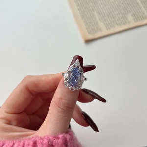 Detailed close-up of a pear-cut lilac gemstone ring with luxury diamond-cluster halo