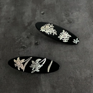 Elegant black oval hair clips with white floral mother of pearl inlay on grey stone