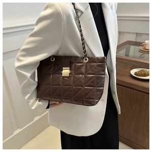 Détail du sac cabas en cuir matelassé marron foncé avec chaîne dorée sur blazer blanc