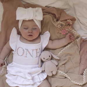 Detail of baby girl first birthday outfit with ONE floral embroidery and bow headband