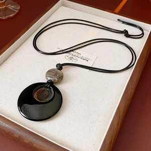 Dettaglio della collana geometrica con anello nero e perla marmorizzata su vassoio