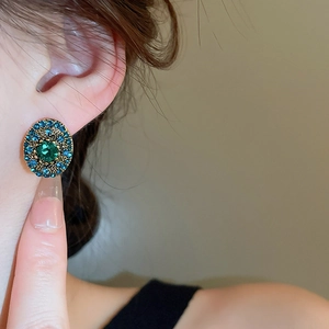 Close-up of vintage oval earrings with green gemstone and blue rhinestones on model