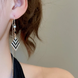 Détail de boucle d'oreille longue avec pendentif losange brillant en strass doré