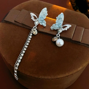 Detail of asymmetric silver butterfly earrings with sparkling rhinestone fringe and pearl