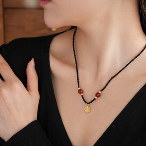 Close-up of red agate beads and gold Fu character pendant on a black woven necklace