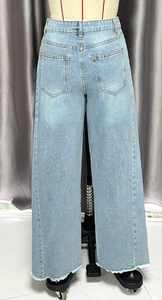 Détail du jean large taille haute en denim bleu clair avec bords inférieurs effilochés