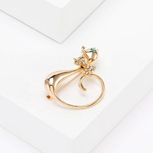 Close-up of golden kitten brooch with rhinestone bow and green eyes on white background