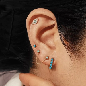 Close-up of gold chain fringe earrings with turquoise eye studs worn by a model