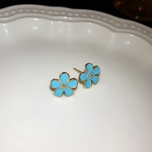 Detailed view of light blue enamel flower earrings on a decorative white ceramic plate