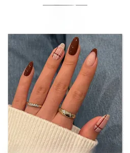 Close-up of French red almond press-on nails with plaid patterns and gold rings
