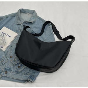 Overhead shot of black nylon dumpling bag on white fabric with lifestyle accessories