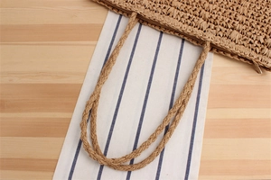 Close-up of woven straw shoulder bag featuring a functional zipper closure and dual straps