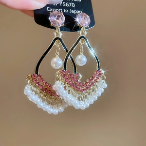 Detail of golden tassel earrings with pink rhinestones and white pearl fringe accents