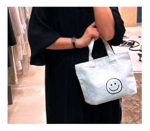 Mini white canvas tote bag with black smiley face pattern carried by a model