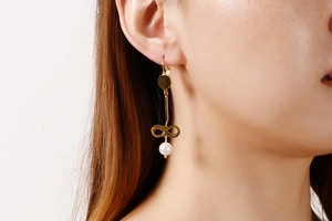 Close-up of long gold infinity earrings with white pearl drop on female model