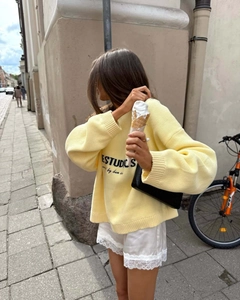 Close-up of a warm yellow oversized knit sweater with ESTUDIOS lettering and soft texture