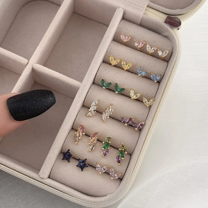 Macro view of colorful zircon star and leaf earrings arranged in a beige jewelry box