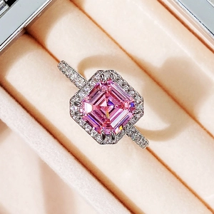 Macro shot of square pink gemstone ring with halo diamonds on beige velvet cushion