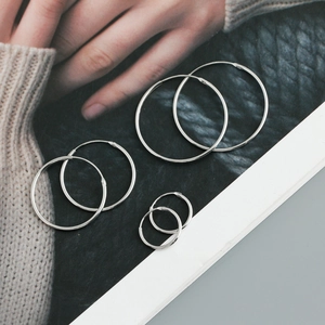 Three sizes of polished S925 sterling silver hoop earrings displayed on a fashion magazine