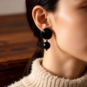 Detail view of black acrylic round earrings with heart relief worn by a model