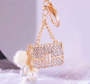 Close-up of golden mini handbag keychain with white rhinestones, resin rose and pearls