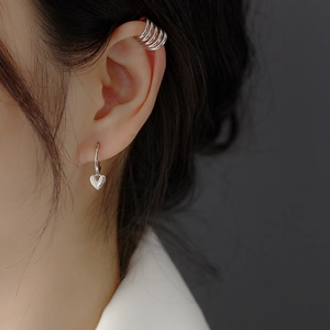 Close-up of silver heart pendant earrings and layered ear cuff worn by a model