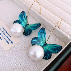 Detailed view of teal butterfly wing earrings with a large white pearl drop