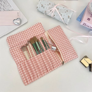 Pink gingham fabric makeup brush roll organizer with ribbon tie on a clean white desk