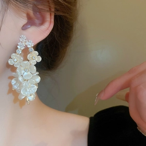 Close-up of elegant white acrylic flower earrings with sparkling rhinestones on model