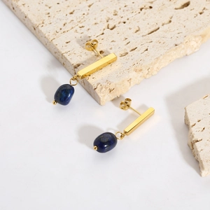 Detailed view of 18k gold earrings with lapis lazuli on beige travertine stone