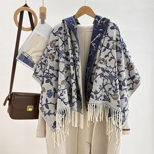 Detail of knit floral jacquard poncho with fringe trim hanging on a wooden hanger
