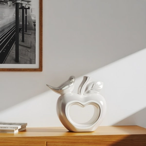 Deko-Apfel und Vogel aus Perlweiß-Keramik auf einem minimalistischen Holzschrank